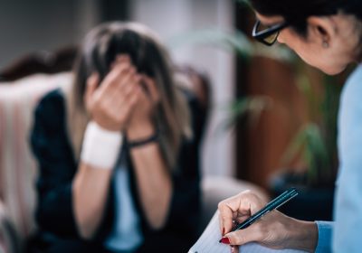 Psychotherapist taking notes during CBT session with mental health patient